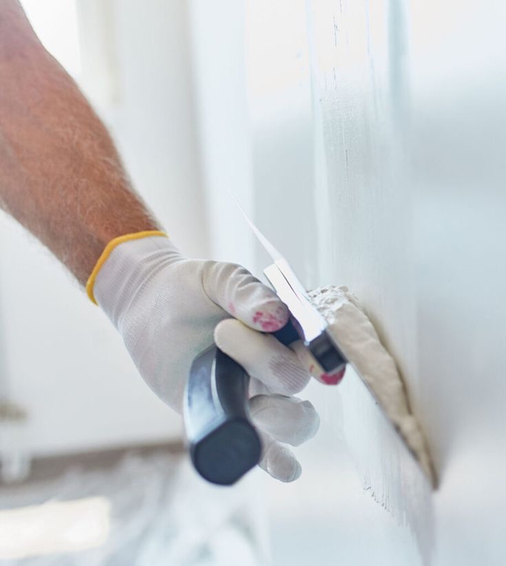Maler trägt Spachtelmasse mit einer Glättkelle gleichmäßig auf eine Wand auf